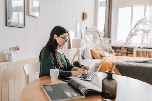 female freelancer typing on laptop while sitting in bedroom